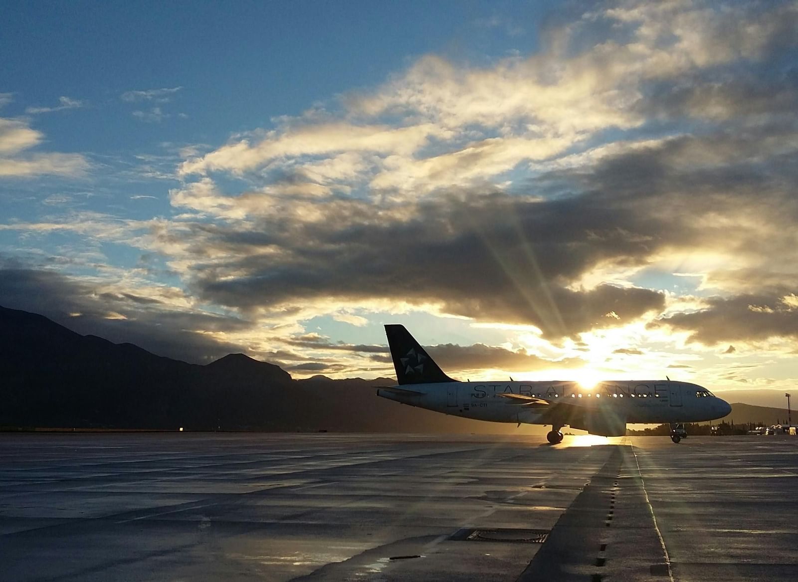 An airplane parked on an airfield at dusk or dawn, with a colourful sky and clouds in the background.