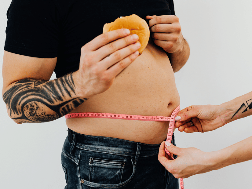 A tape measure being wrapped around a man's waist to measure his body fat