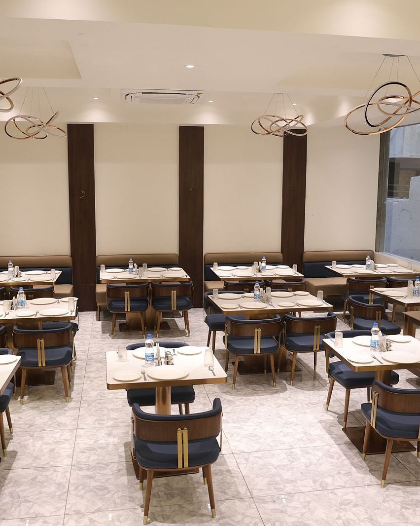 A brightly lit dining area at Lords Eco inn Jamnagar Maheshwari Nagar with multiple tables chairs and stylish lighting.