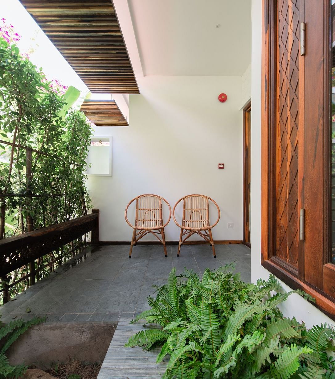 A balcony with lush green trees and comfortable wooden chairs to relax on - Alibu Resort Nha Trang