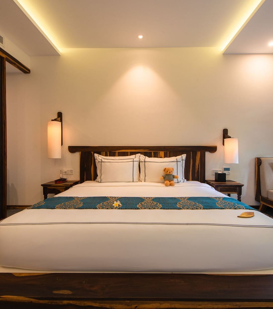 A front view of a large white bed with a teddy bear on it with a balcony to the right - Alibu Resort Nha Trang