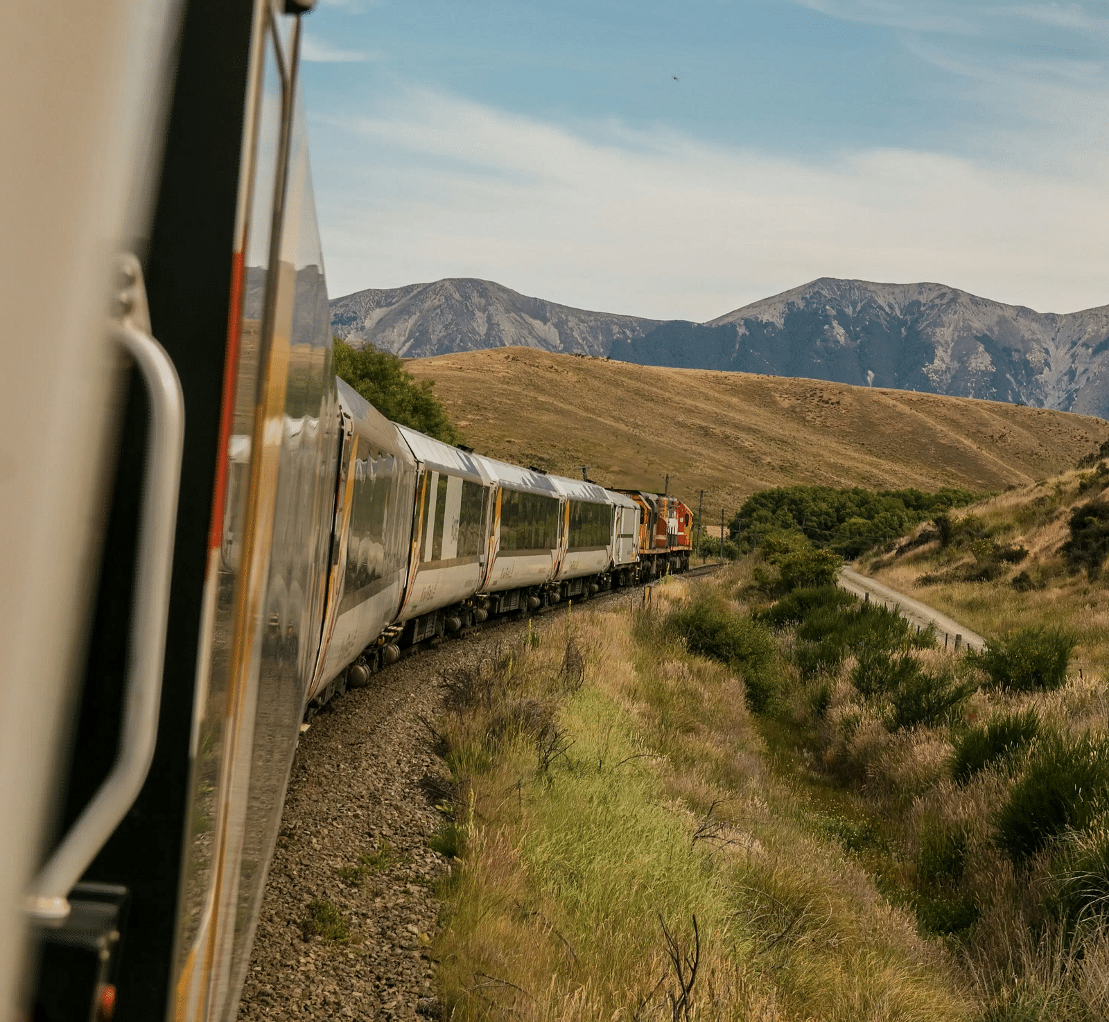 A side view of a passenger train curving into an empty grassland during a bright afternoon.