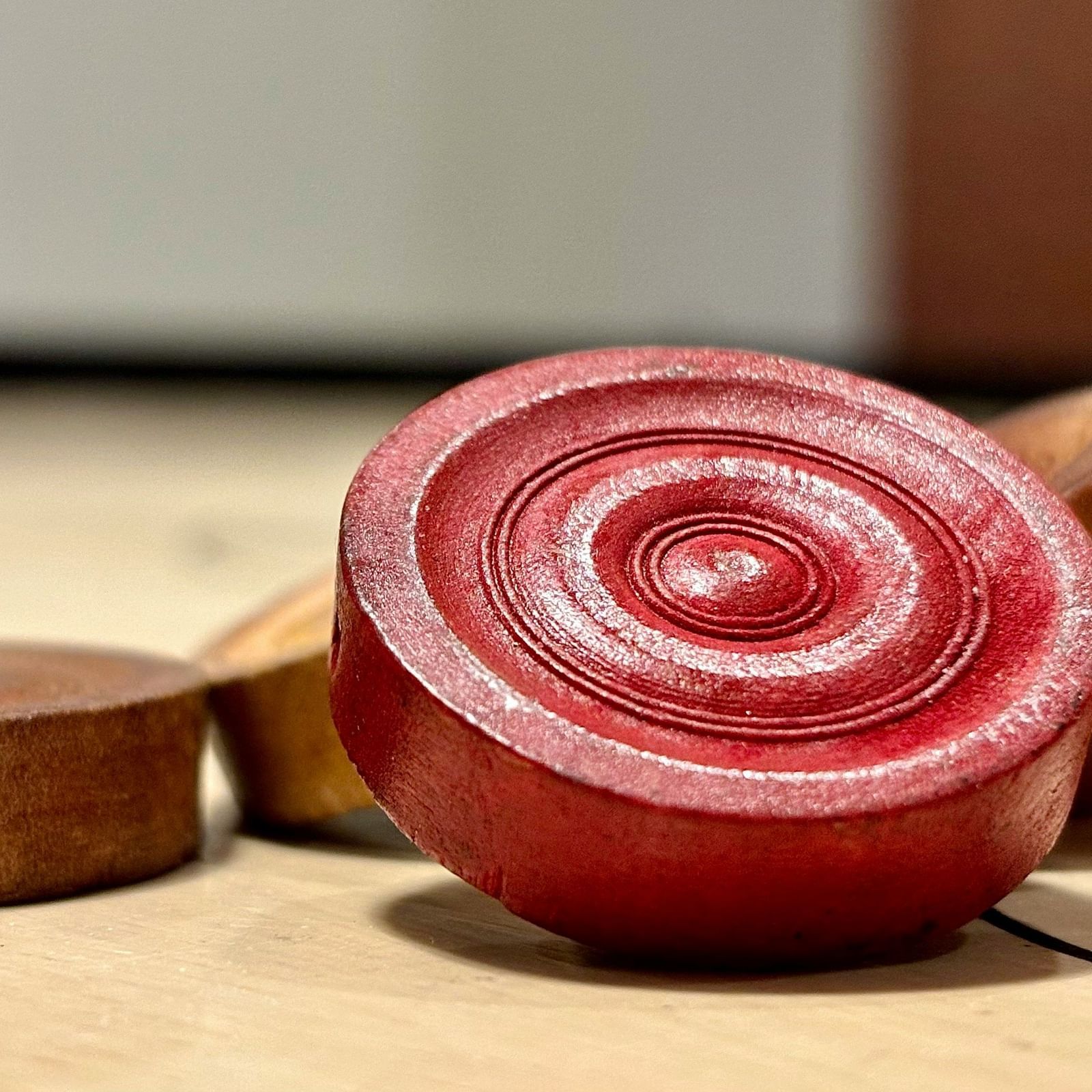 A red carrom man placed on beige carrom men on a carrom board.