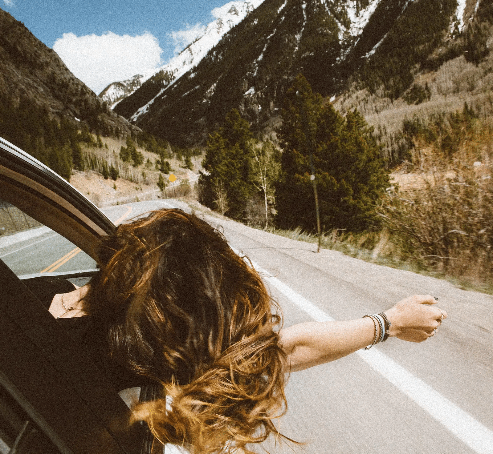 A girl siting in a car with her hand wide open feeling the gentle breeze.
