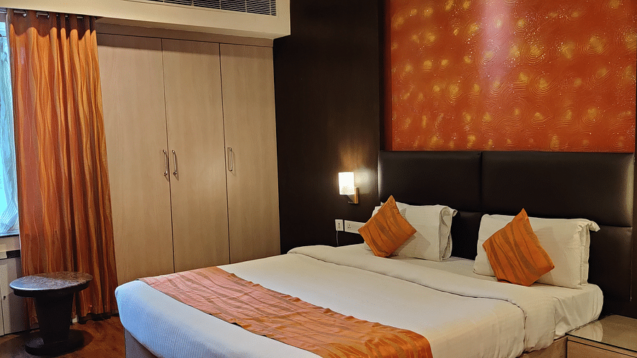 A modern hotel room at Renest Tirupati features a king-sized bed with decorative pillows and a runner, bedside lighting, a window with curtains, and a wardrobe