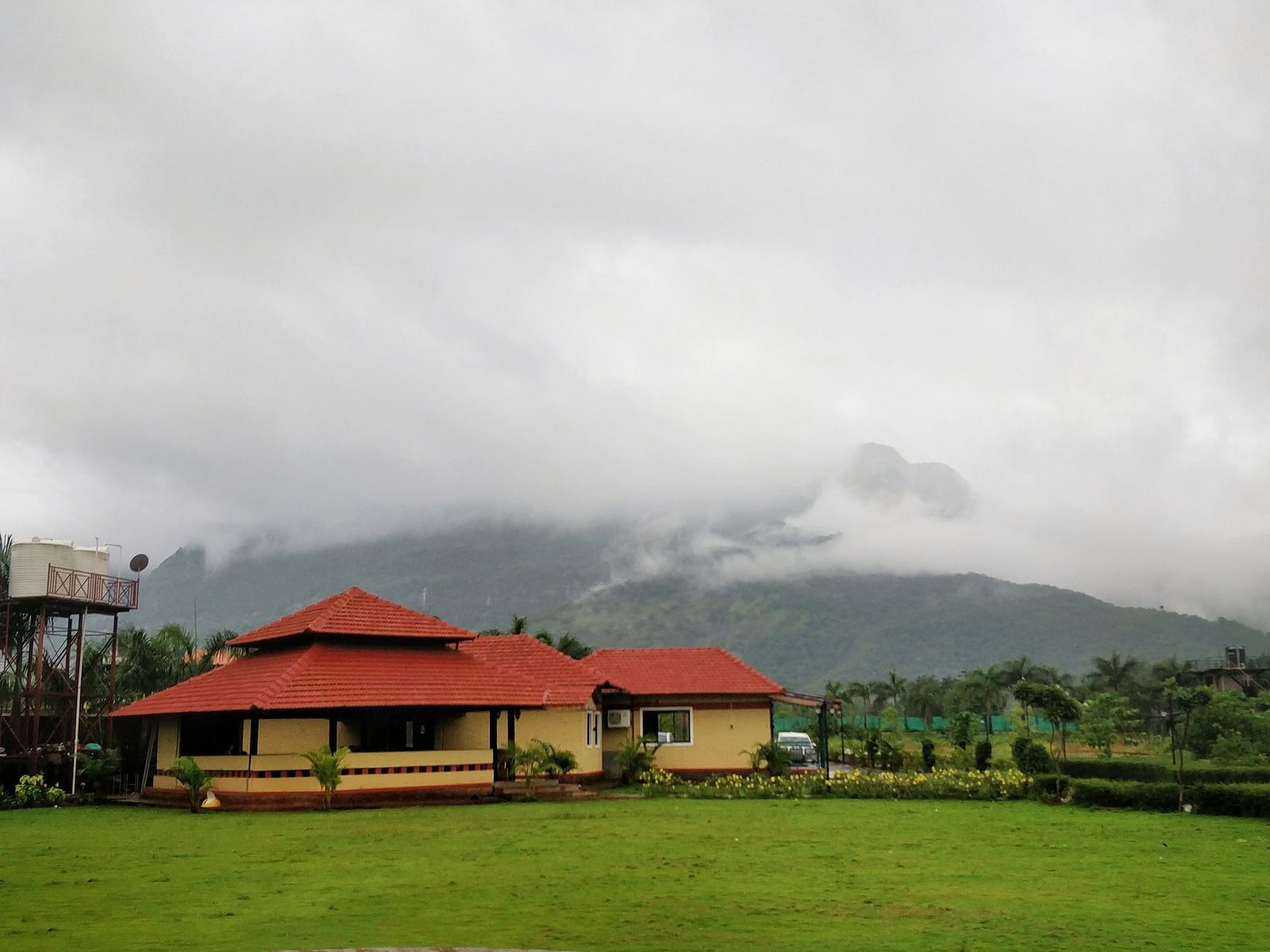  A lush green field with a house and trees in the background, under a grey and cloudy sky | The Kanila Resort