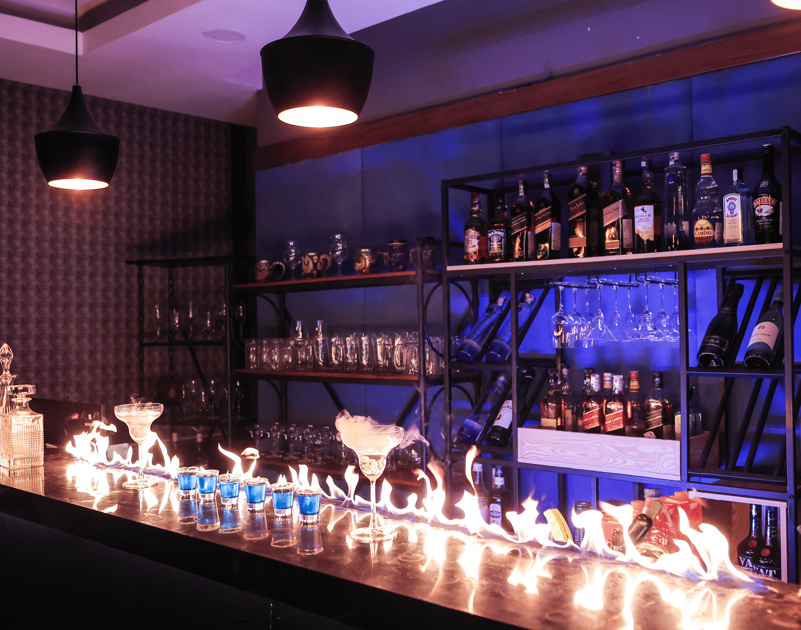 Stylish bar area with bottles on shelving, featuring a long, dramatic flame or dry ice effect across the counter at Hotel Hukam's Lalit Mahal.
