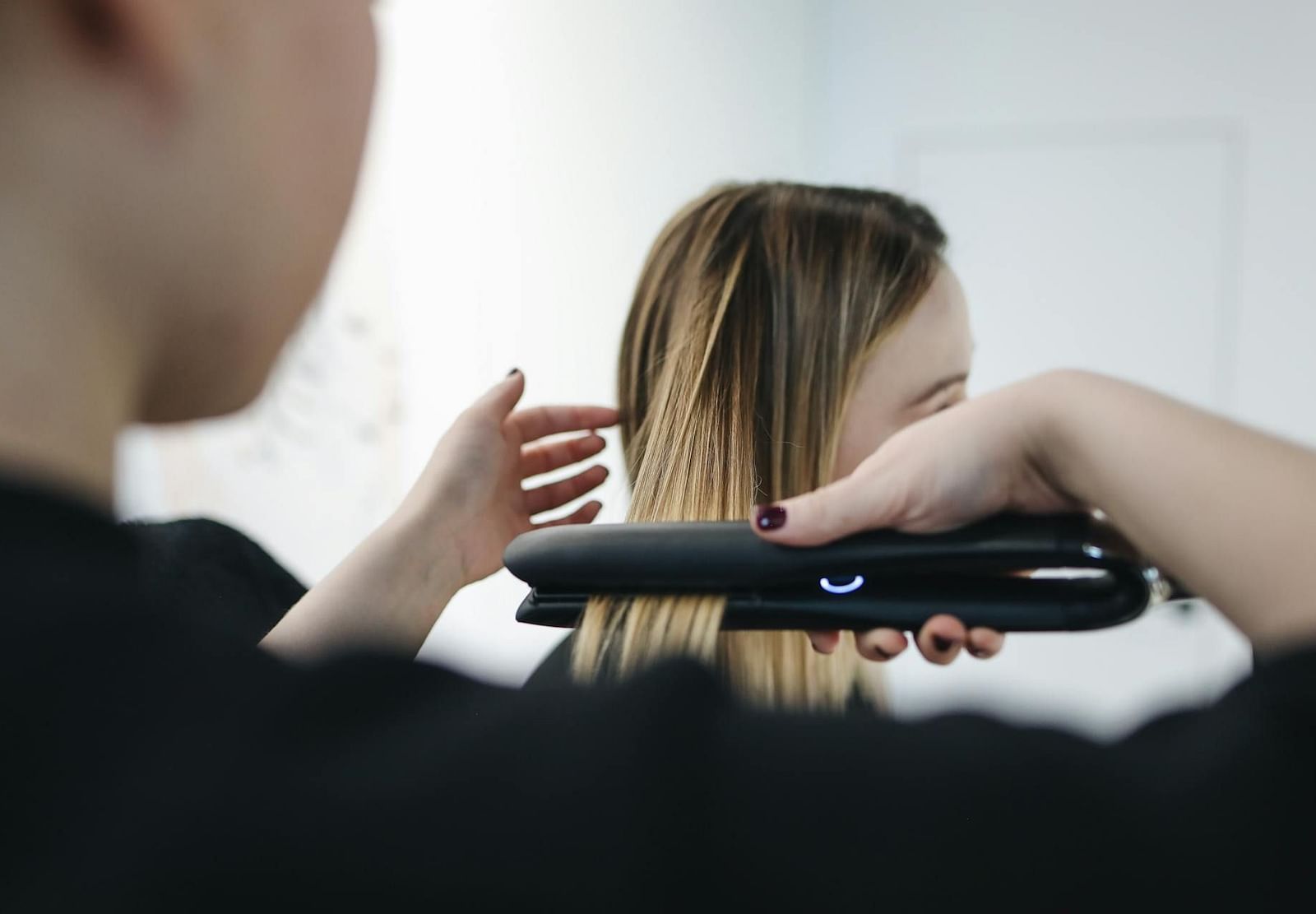 A woman sitting while another person straightens her hair with a hair straightener