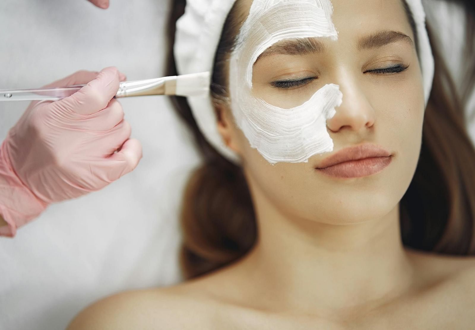 A woman with here eyes closed receives a facial mask treatment.