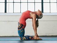 A woman performs the Camel Pose on a yoga mat, arching her back and grasping her heels