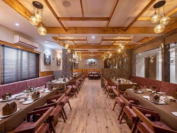 A dining area with multiple tables and chairs set for meals along a corridor with a wooden theme at Angel Lords Eco Inn Amreli.
