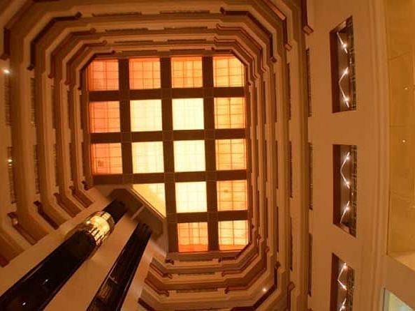 Interior view of a hotel featuring corridors illuminated by warm yellow lights, captured from an upward angle.