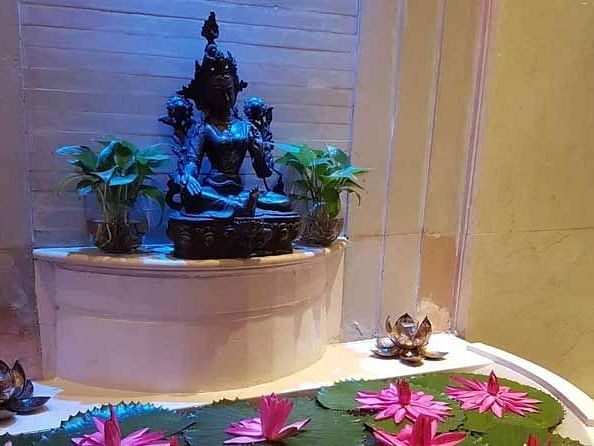 A view of a hindu idol with plants on both sides and lotuses before.