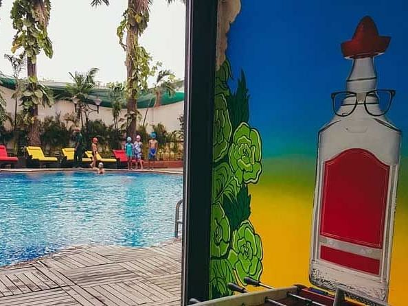 View of a colourful wall and swimming pool with trees and colourful chairs in the background.