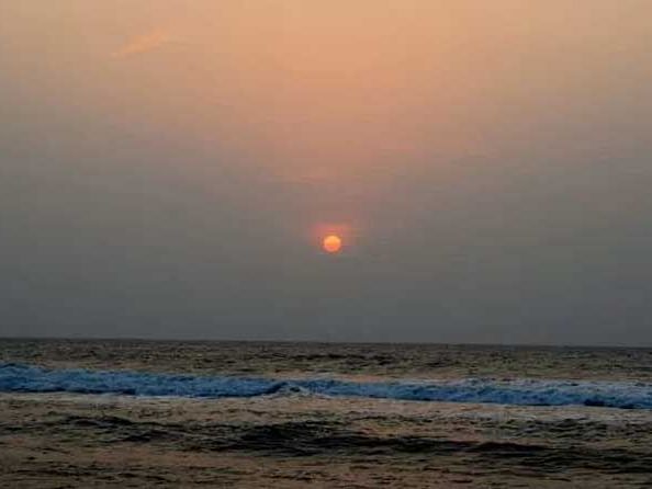 A scenic view of a sunset filling the sky with shades of orange and blue with ocean waves beneath.