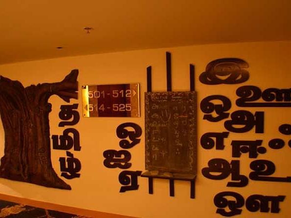An image of a wall featuring room number plate along with Tamil letters besides it