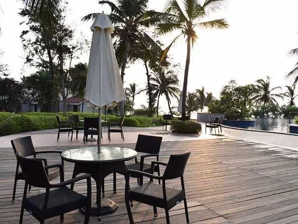 A view of the wooden deck, table, chairs with swimming pool in the background surrounded by beautiful coconut trees.