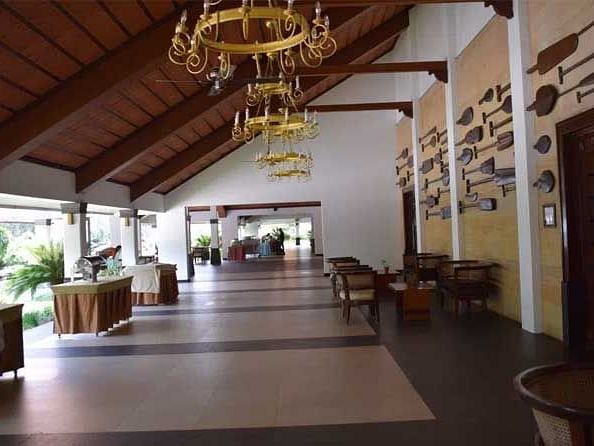 A view of a beautiful corridor with tables, chairs, chandelier and beautiful wooden structures on the wall.