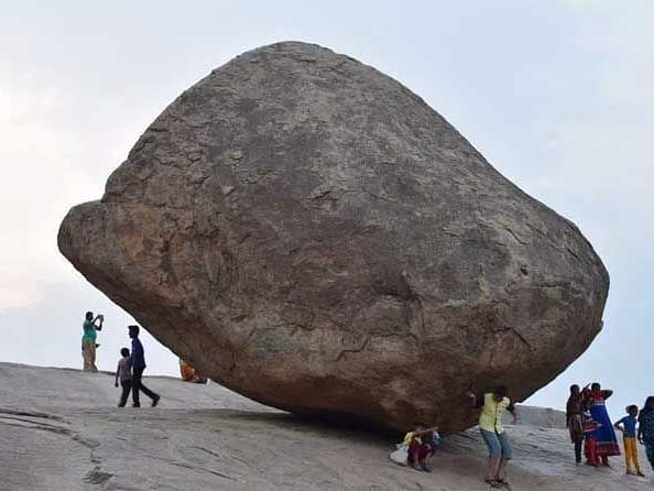 A large, balanced stone standing precariously, surrounded by people.