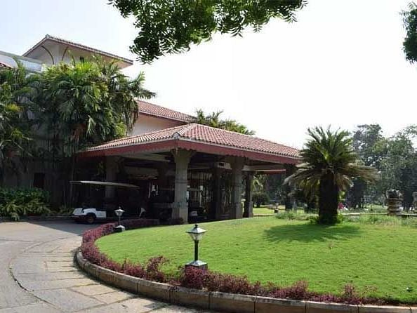Facade shot of a hotel entrance with a beautiful front garden and a lot of trees with a clear blue sky background.