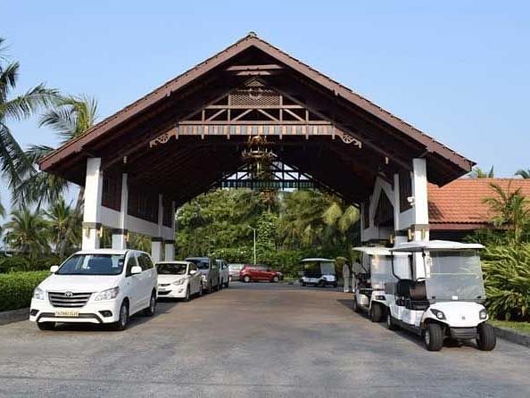 A big wooden entrance with a lot of vehicles parked underneath it and trees in the background.