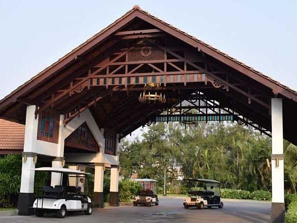 A big wooden entrance with vehicles parked underneath it and trees in the background.