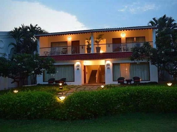 Front shot of a building with bright lights on and garden and trees infront of it.