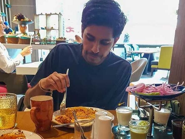 A person eating his food while sititng on the sitting with buffet arrangement in the background.