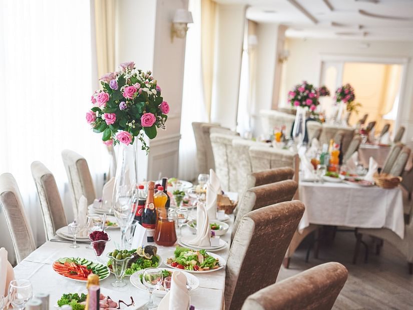 A wedding table with flower decors, chairs, food items, and beverages in a lively setting