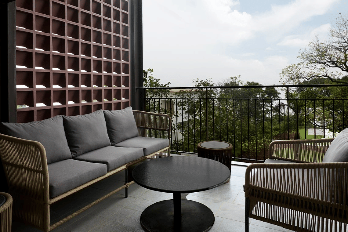 Outdoor balcony area with modern woven-rope patio furniture, including a sofa and chairs, and a black coffee table, overlooking trees.