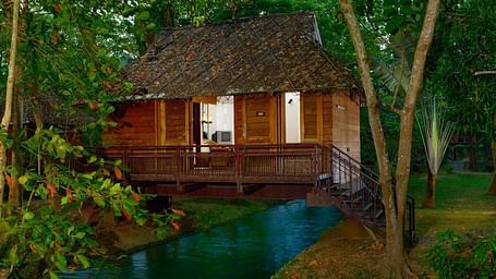 A cottage placed in lush green setting with a small stream of water flowing below it