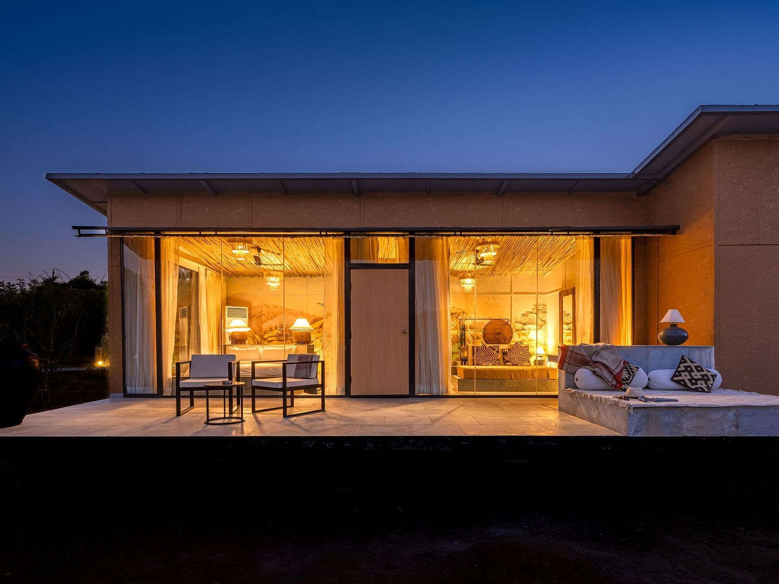 A facade image of a room with bright lighting and greenery around - Utsav Camp Sariska.