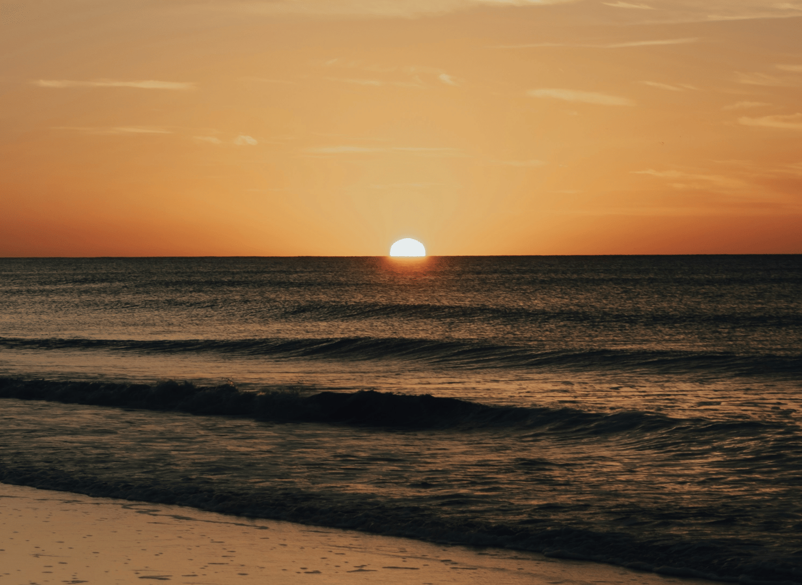 A sun setting over the beach, seen from the shore.