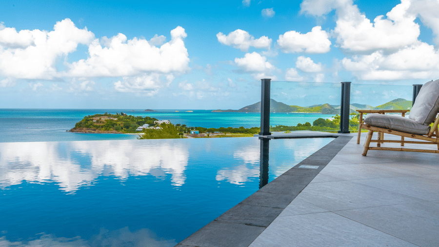 A pool at Tamarind Hills Resort and Villas, Antigua, with two lounge chairs at poolside and an ocean view.