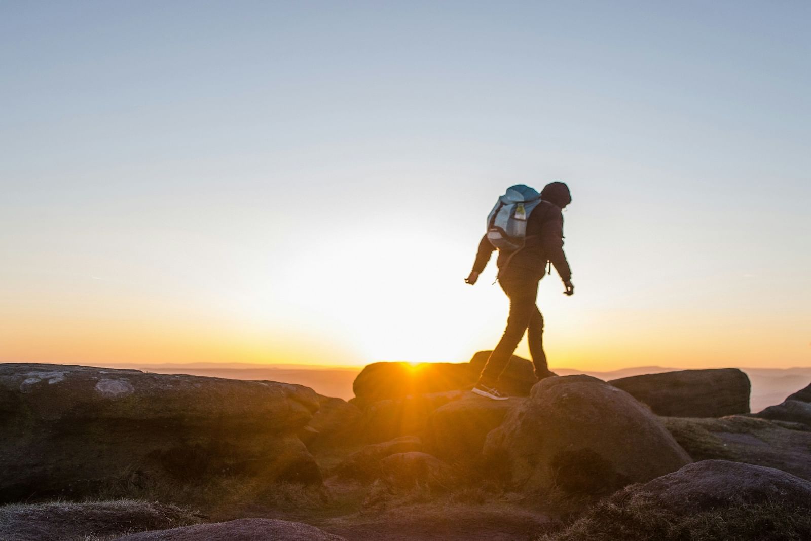 Image of a man with a backpack walking on the rocks with bright sun in the background