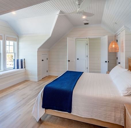 Bedroom with sloped ceilings, blue bed runner, and woven pendant light | Abaco Inn