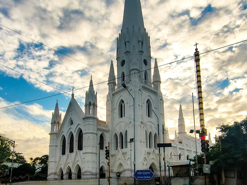 A low-angle shot of a white cathedral with a tall, pointed spire set against a dramatic sky with clouds.