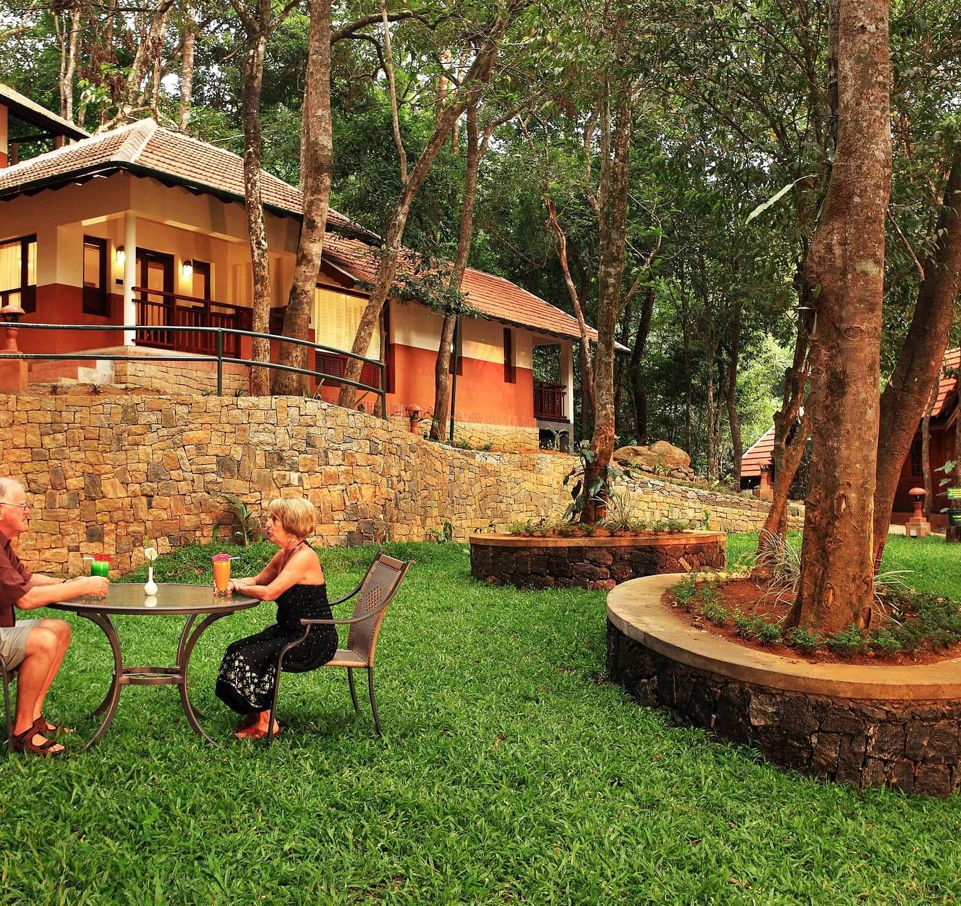 A couple sitting at a dining table outside the villa amidst greenery | Vythiri Resort, Wayanad