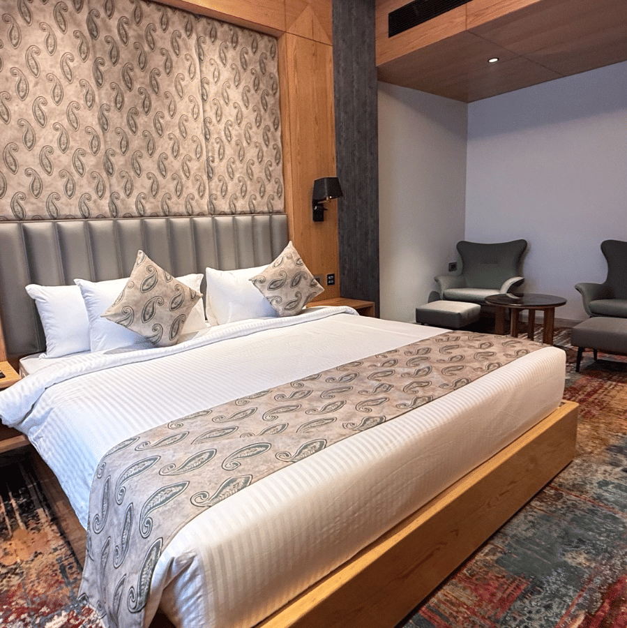 A modern bedroom featuring a king-sized bed with a patterned headboard and vibrant multicoloured carpeting at Ananta Express, Katra.