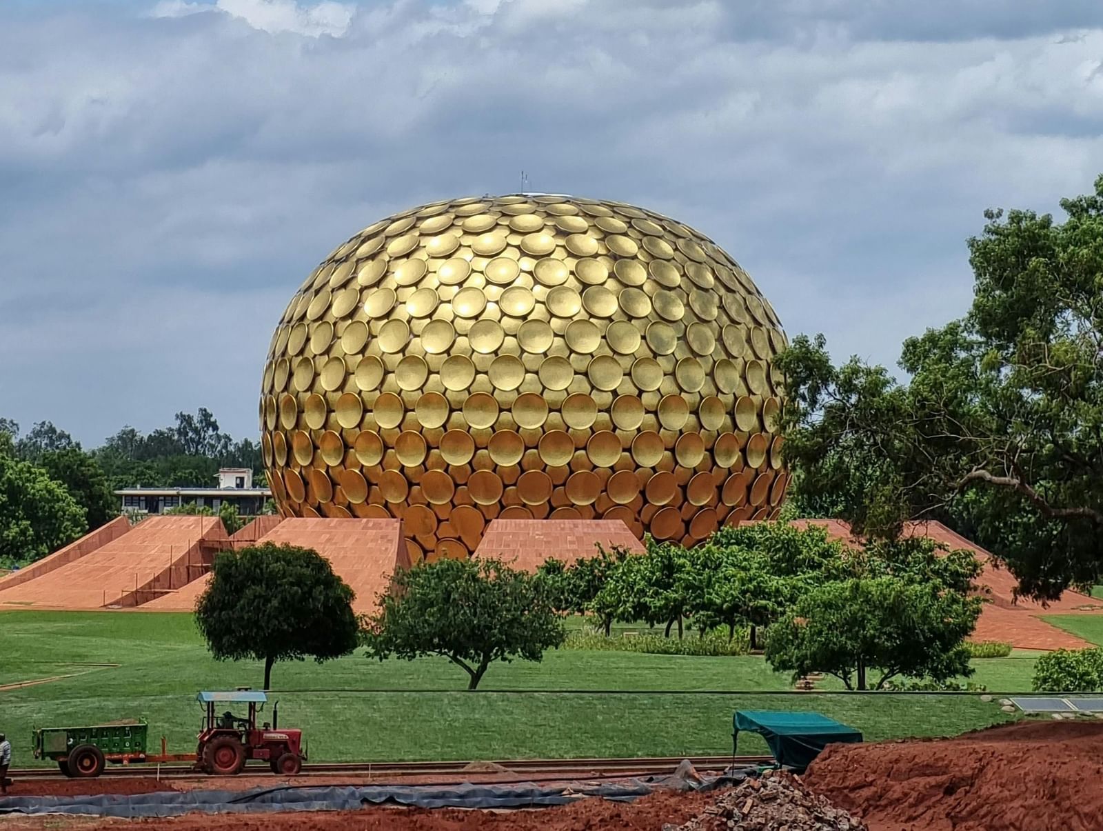 Circular patterned golden dome of Auroville Temple in Puducherry amidst the greenery and under the blue sky.