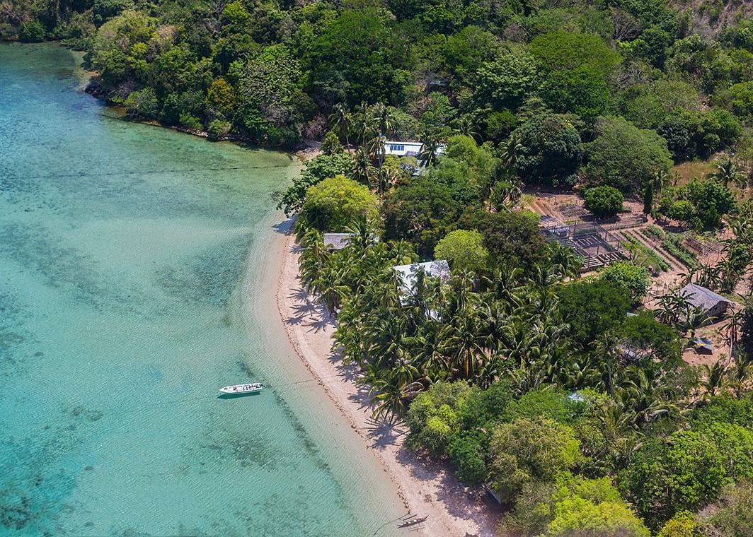 Coastal aerial view showing turquoise water, beach, and greenery at Flower Island Resort.