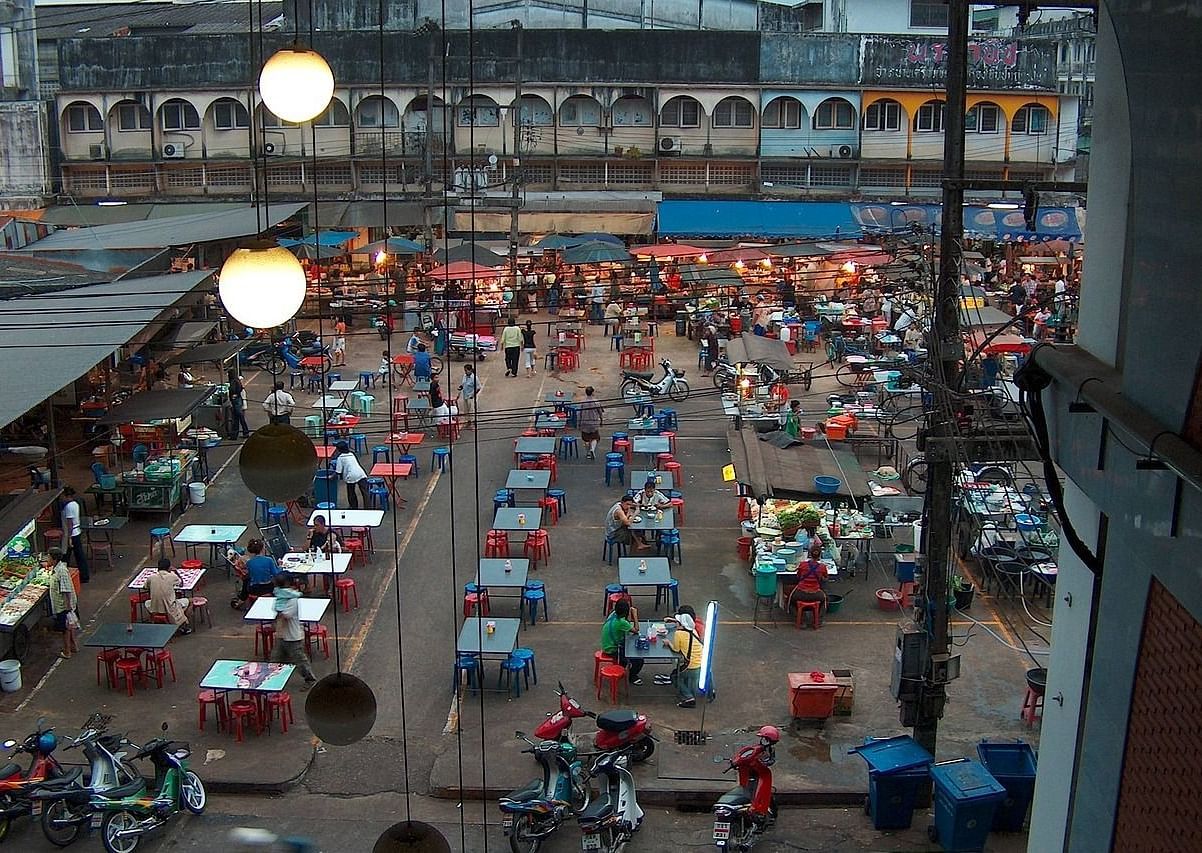 An overview of a night market as seen aerially with stalls and people sitting on a table eating in view.