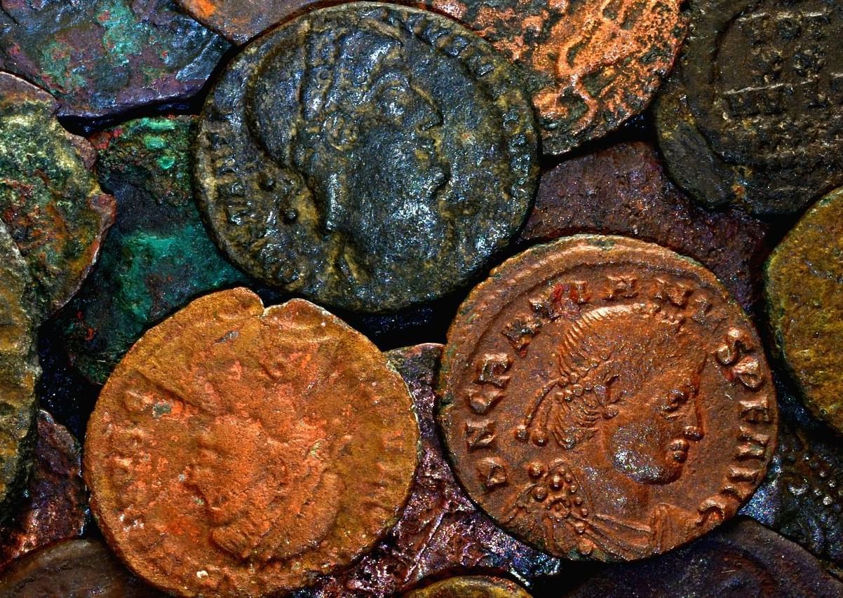  A close-up, high-angle shot of several ancient, corroded coins, with two coins in the foreground showing detailed portraits.