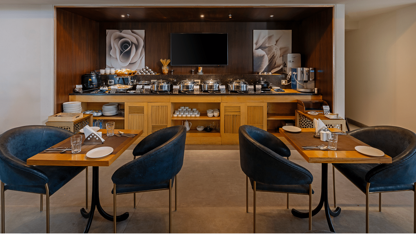 A stylish dining area at Hotel Saket 27, offering comfortable seating and a buffet counter in the background.