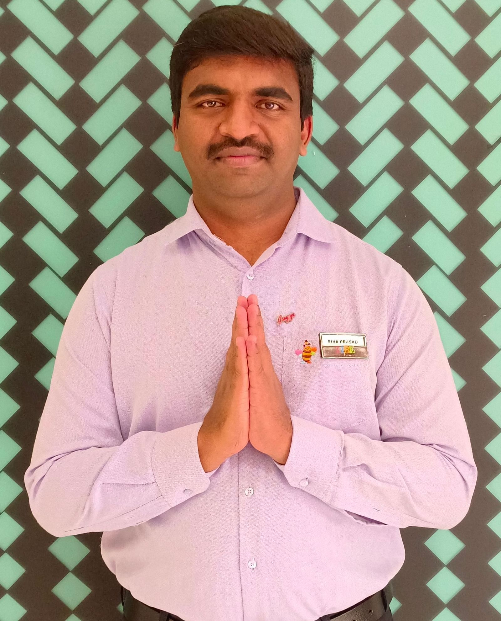 Mr. Siva Prasad stands with poise against a backdrop featuring a repeating pattern.