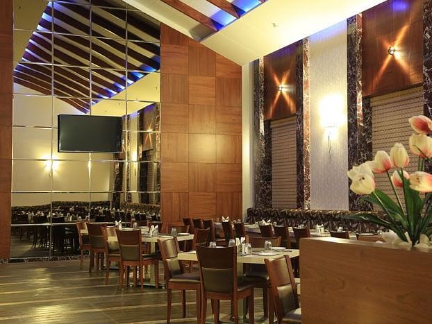 A grand dining area with high ceilings, wooden panel walls, and soft lighting for an upscale experience. - Dhanalakshmi Srinivasan Hotels, Perambalur