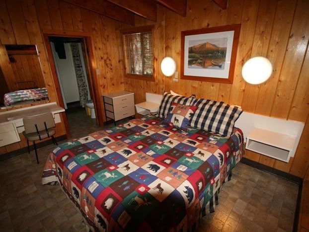 The interior of a cozy cabin bedroom featuring a patterned bedspread, wooden walls, and framed artwork | Red Squirrel