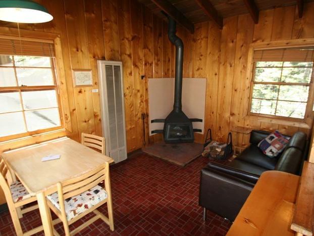 The interior of a cozy cabin features knotty pine walls, a stone fireplace, and a dining area with a wooden table and chairs | Deer I