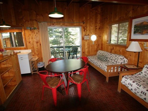 The interior of a spacious cabin features a living area with a sofa and armchairs, a dining area with a red table and chairs, and large windows offering a view of the outdoors | Gray Squirrel