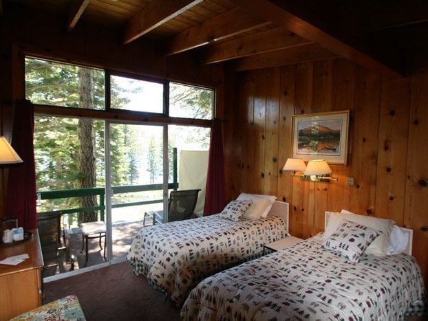 A bedroom with two beds, wood-paneled walls, and large windows offering a view of the surrounding nature